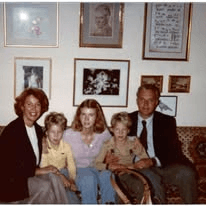 A family of five seated on a couch beneath framed pictures.