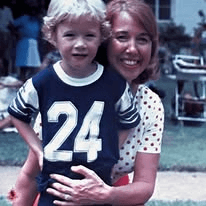 A woman in a polka-dot top holding a blond child wearing a number 24 jersey.