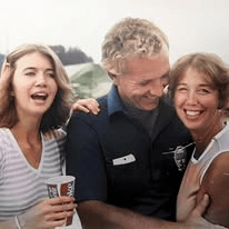 Two women laughing beside a man in a uniform shirt outdoors.